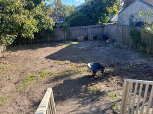 Backyard cleared back to bare soil with a wheelbarrow, ready for new turf.