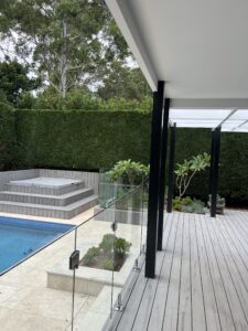 Pool with glass fencing, spa steps and courtyard planting beside a hedge.